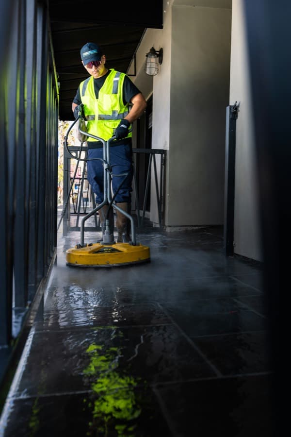 Worker in a high visibility vest pressure washing a walkway
