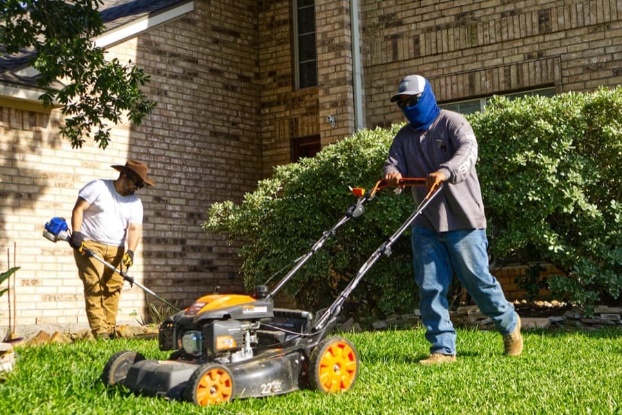 Two crew members mowing and trimming a lawn